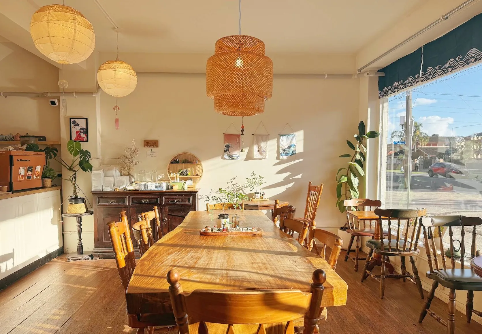 Sunlit café interior with a long timber table and paper lanterns
